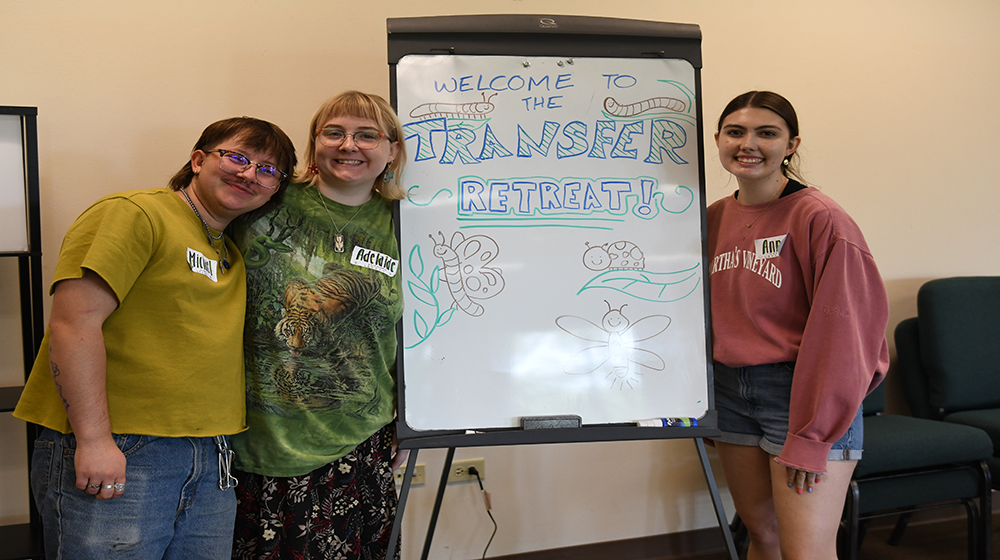 Three students by a sign that says 'Transfer Retreat'